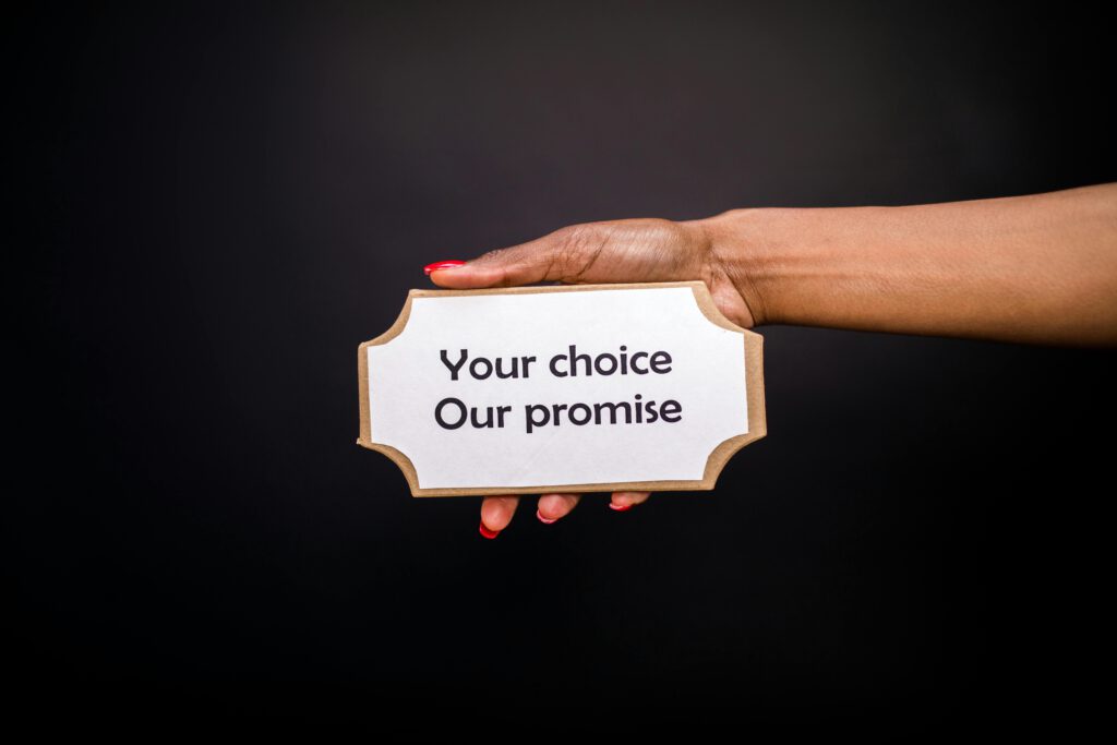 A hand holds a sign saying 'Your choice, Our promise' against a dark background.